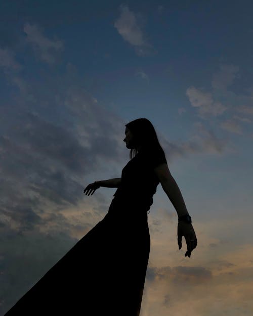 From below side view of woman with long hair spreading hands while enjoying evening time