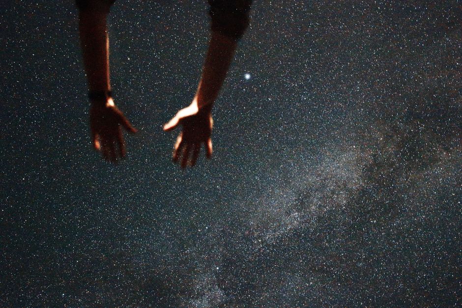 Silhouetted hands reaching towards a starry night sky