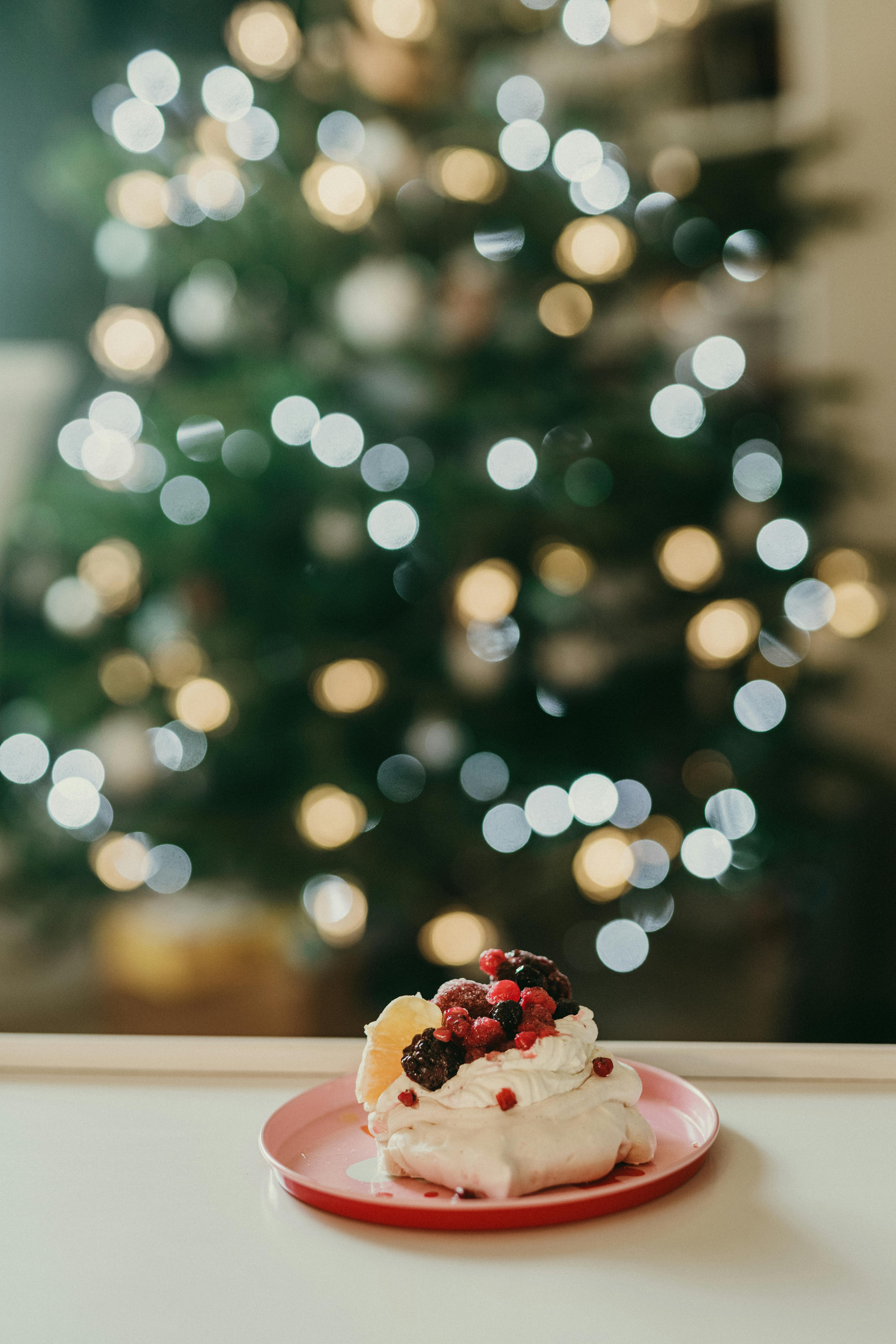Festive dessert with berries on plate, blurred Christmas tree lights in background.