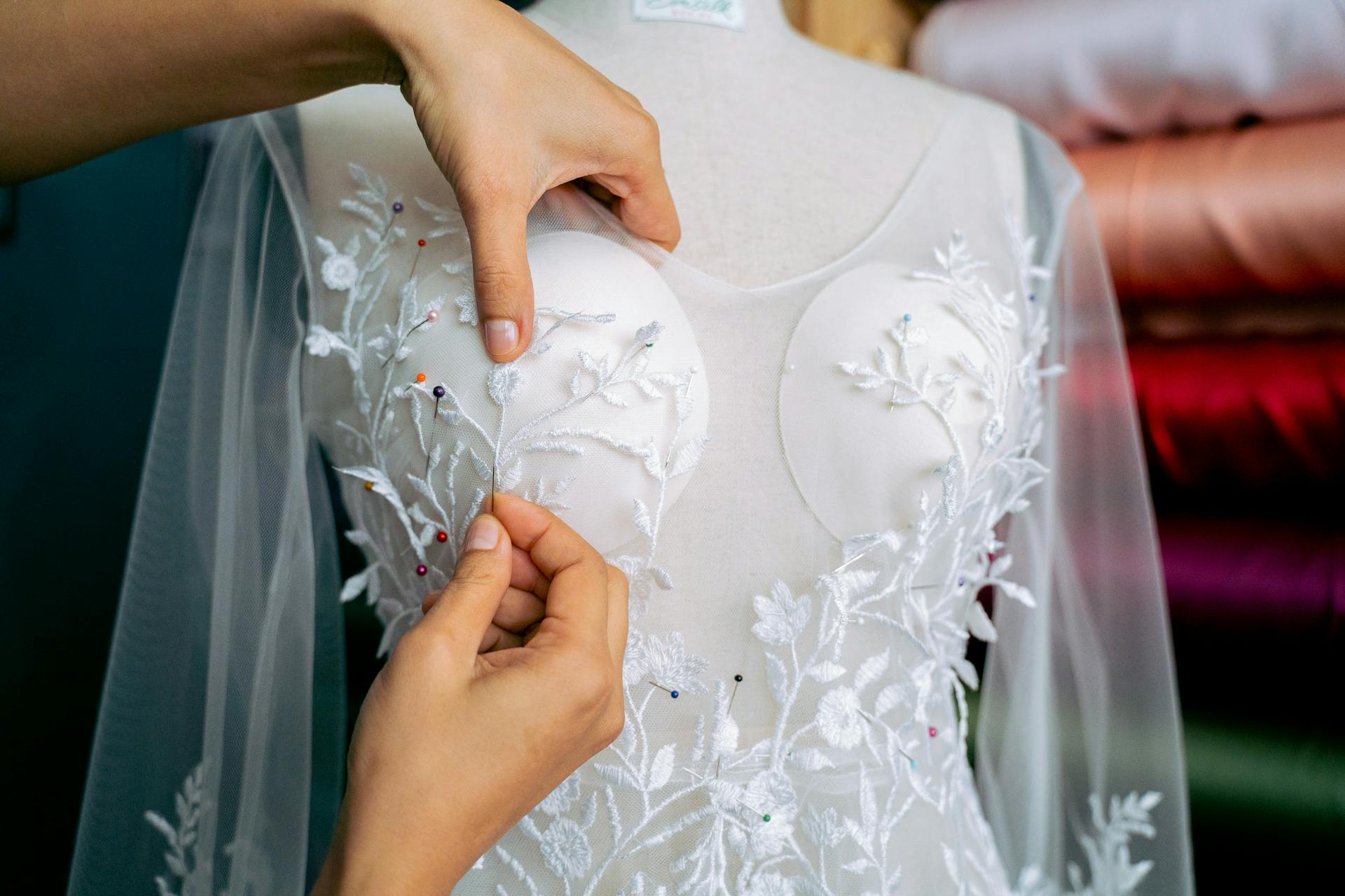 Detailed close-up of hands adjusting lace on a wedding dress in a fashion atelier.