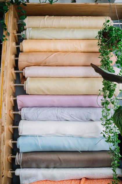 Các cuộn vải nhiều màu xếp trên giá tại cửa hàng vải, thể hiện đa dạng chất liệu cho xưởng may
