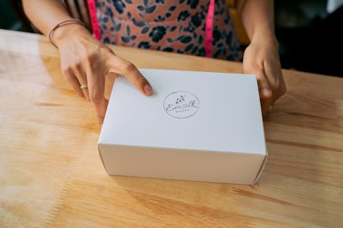 Free Close-up of hands holding a white branded box on a wooden table. Stock Photo