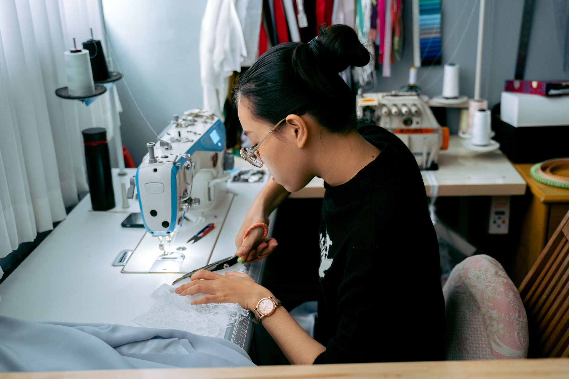 A focused seamstress cutting fabric in a workshop with a sewing machine.