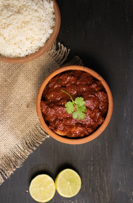 A bowl of deep red carne adovada with tender chunks of pork submerged in thick red chile sauce, garnished with chopped cilantro.