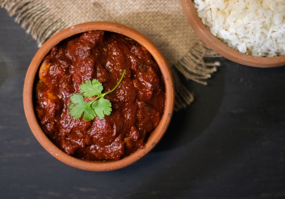Deep red madras curry in a clay bowl with fresh cilantro garnish