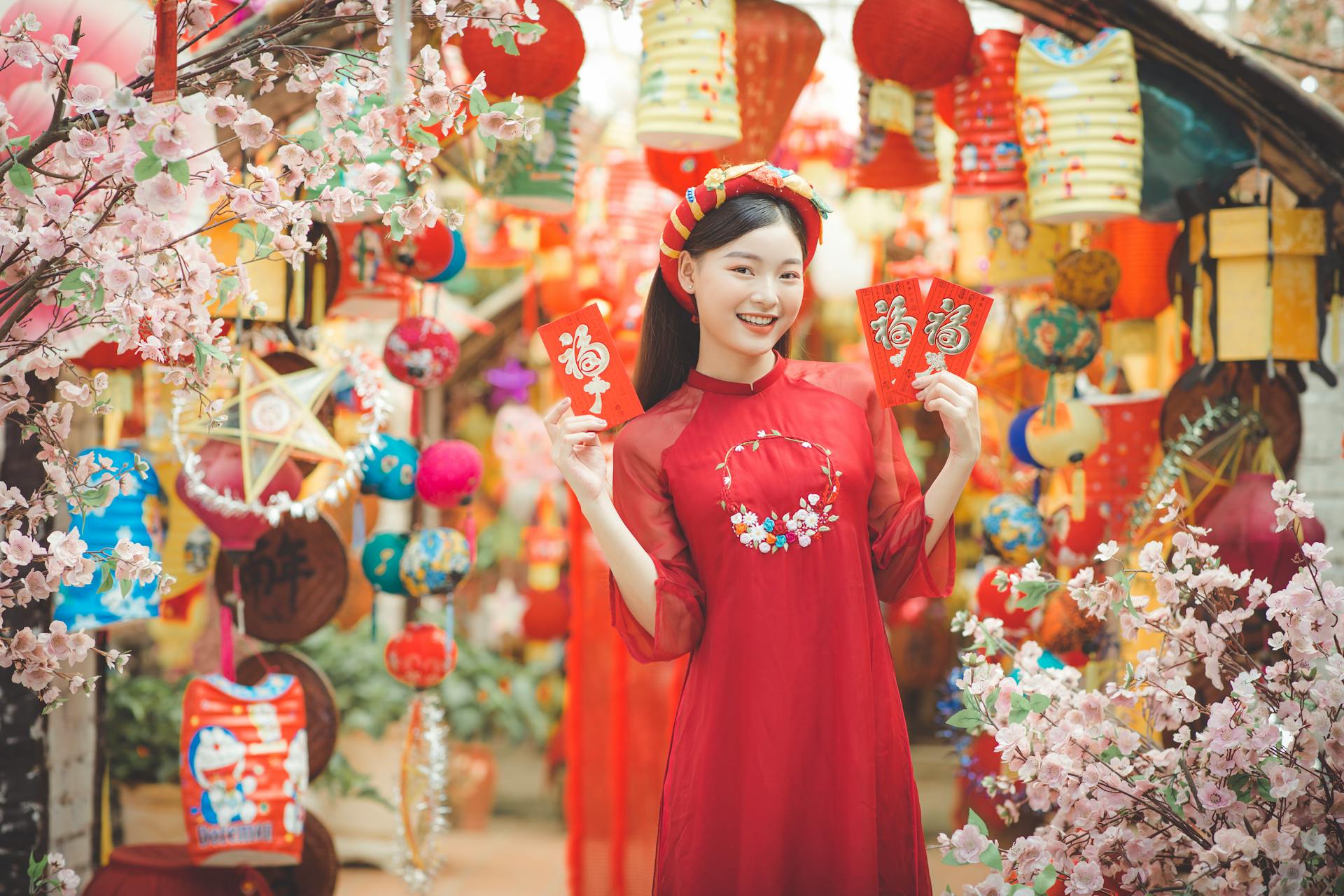 East Asian woman in traditional dress holds red envelopes during Vietnamese New Year celebrations.