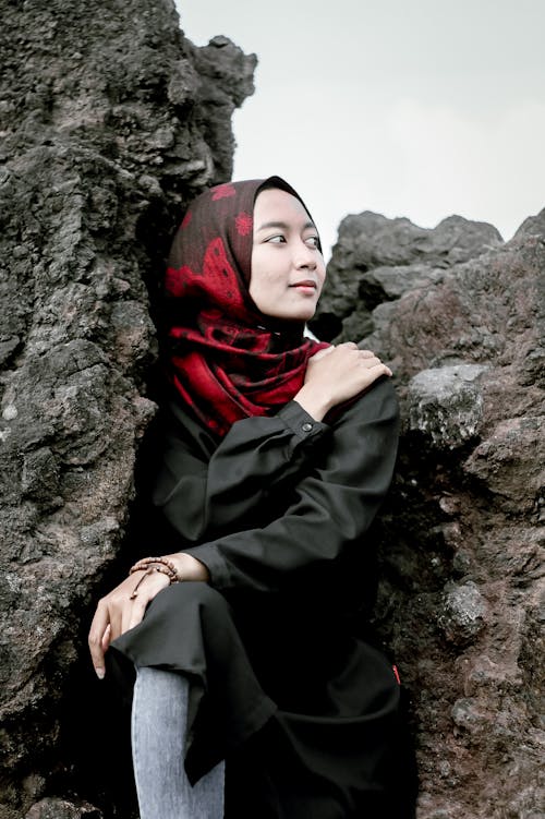 岩の上に座っている黒いコートの女性