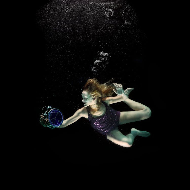 A Woman Holding A Clock Underwater