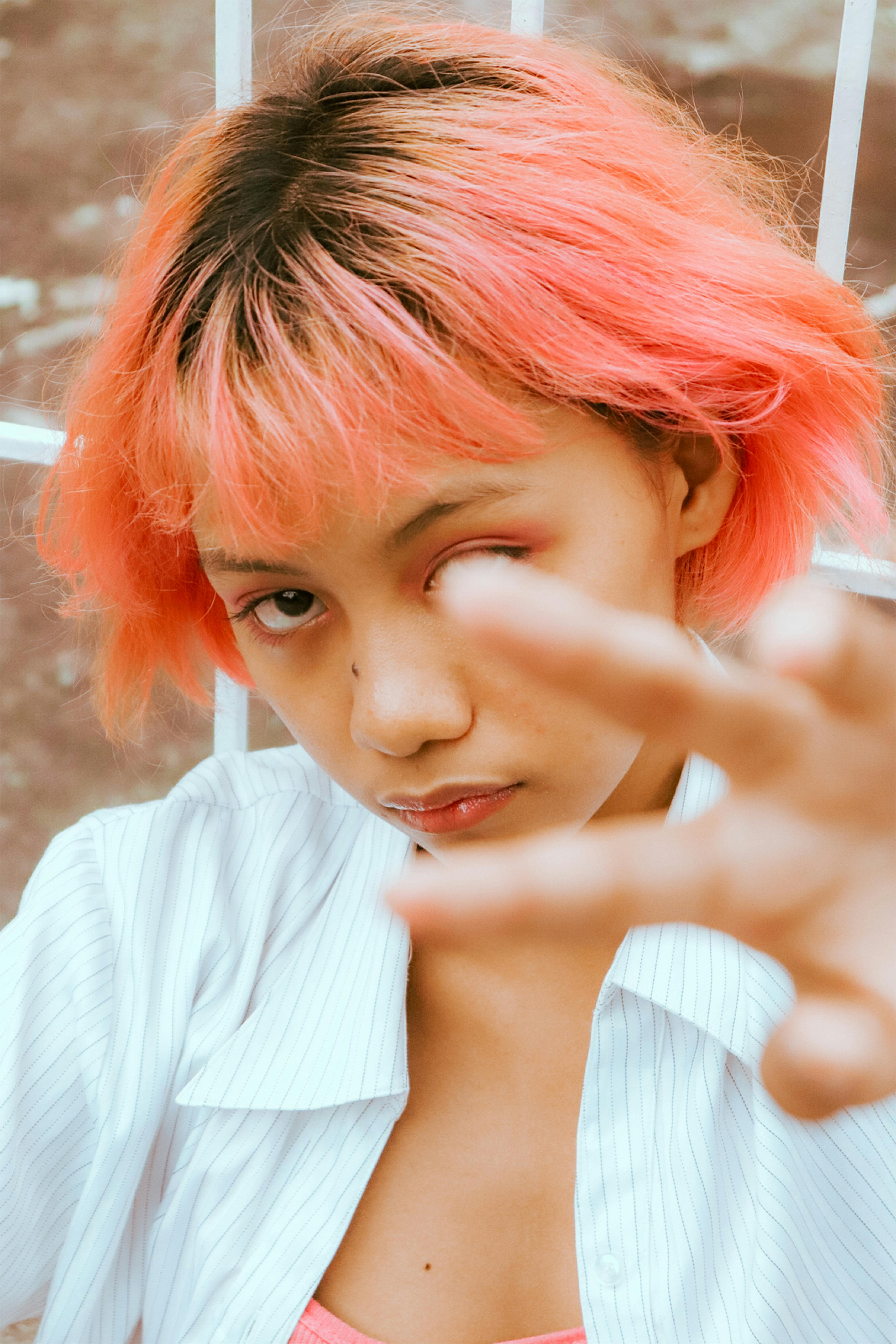 Close-up portrait of a young woman with dyed pink hair reaching towards the camera.