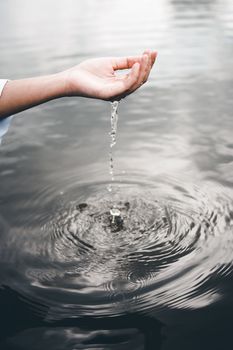 Crop anonymous female pouring clear water from hand into rippling splashing river at daylight