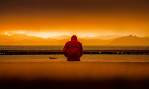 Orang Yang Mengenakan Hoodie Merah Duduk Di Depan Perairan