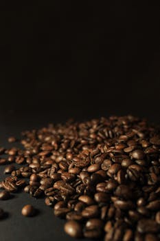 A pile of rich, dark roasted coffee beans on a dark background, perfect for your caffeine-themed projects.