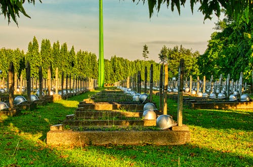 Various tombstones with military hardhats located on grassy ground in national main heroes cemetery against green trees and tall structure