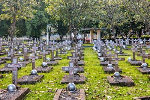 Abundance of tombstones with crosses and military helmets located on grassy ground on national main heroes cemetery with structure