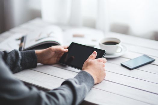 Adult holding a tablet at a minimalist workspace with coffee and a smartphone nearby.