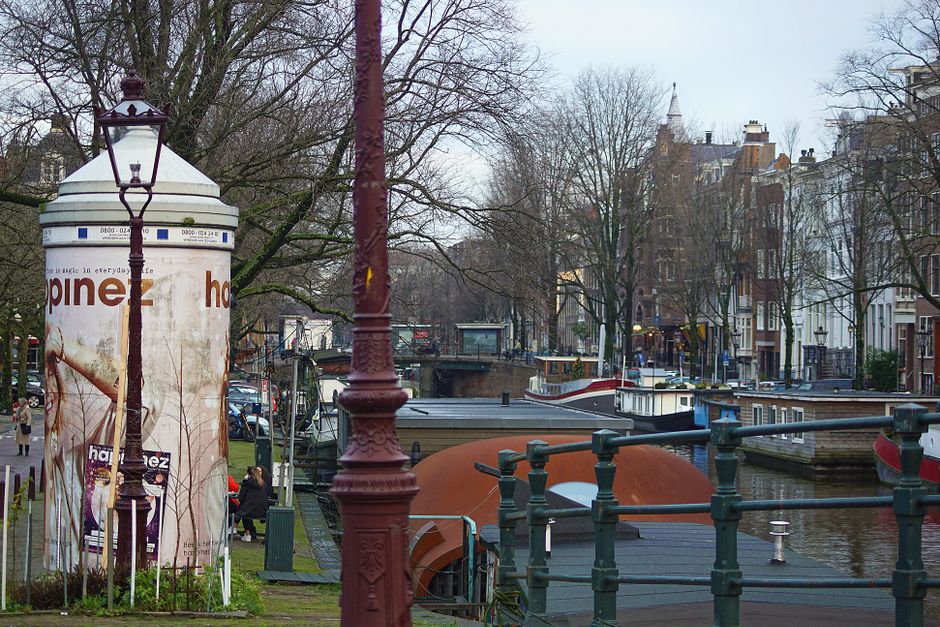 Charming view of Amsterdam's canal with traditional boats and historic buildings under a cloudy sky.