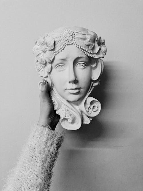 Black and white of crop unrecognizable female in warm clothes demonstrating handicraft plaster sculpture