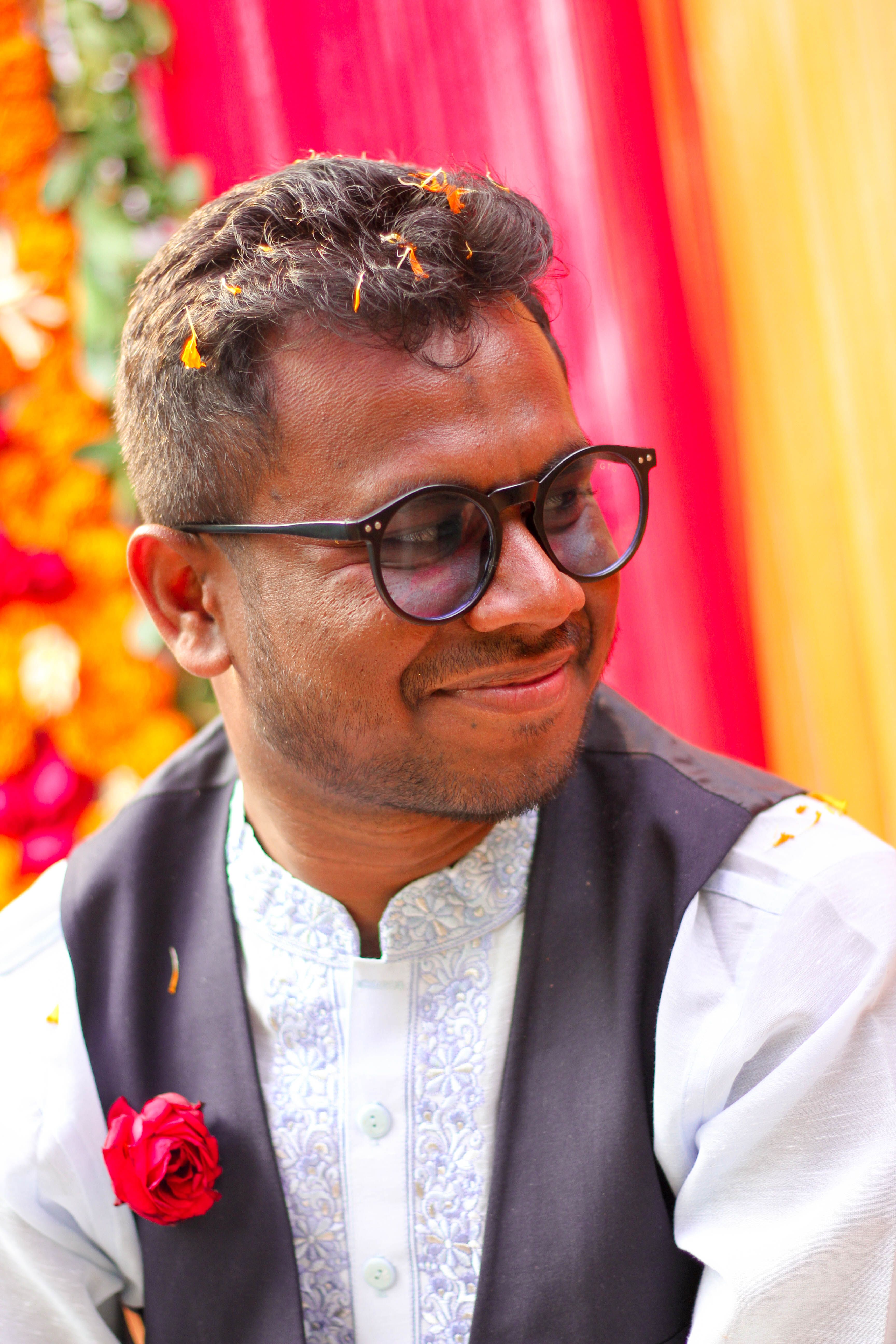 Smiling Indian man in traditional attire at a vibrant wedding ceremony.