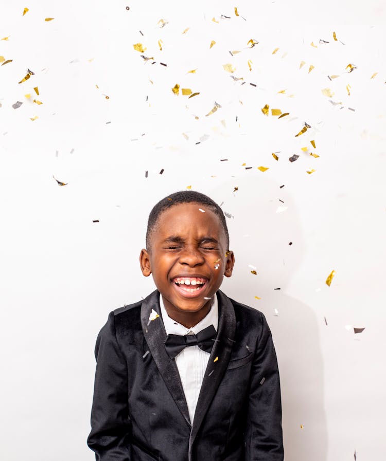 A Cute Boy Wearing A Black Suit Jacket And Bow Laughing Under A Falling Confetti