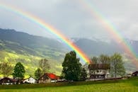 在奥地利蒂罗尔州风景如画的施利特村上空，一条充满活力的彩虹矗立着，四周环绕着郁郁葱葱的绿色植物和山脉