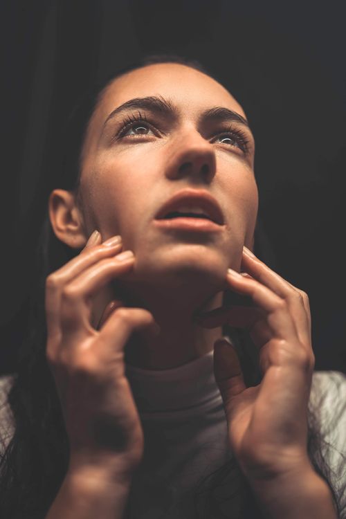 Free Close-up portrait of a woman with a thoughtful expression, touching her face with both hands. Stock Photo