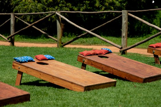 Wooden cornhole boards with colorful bean bags on a green lawn during a sunny day outdoors.