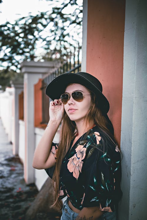 Trendy young female millennial adjusting sunglasses near fence in