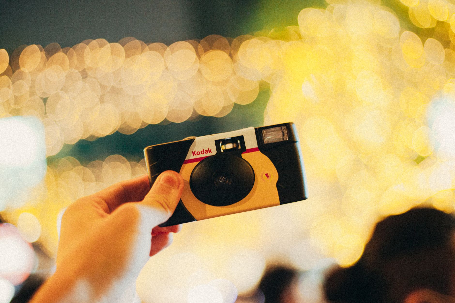 A disposable camera held up against a sparkle of reception lights — the tactile object the digital category replaced