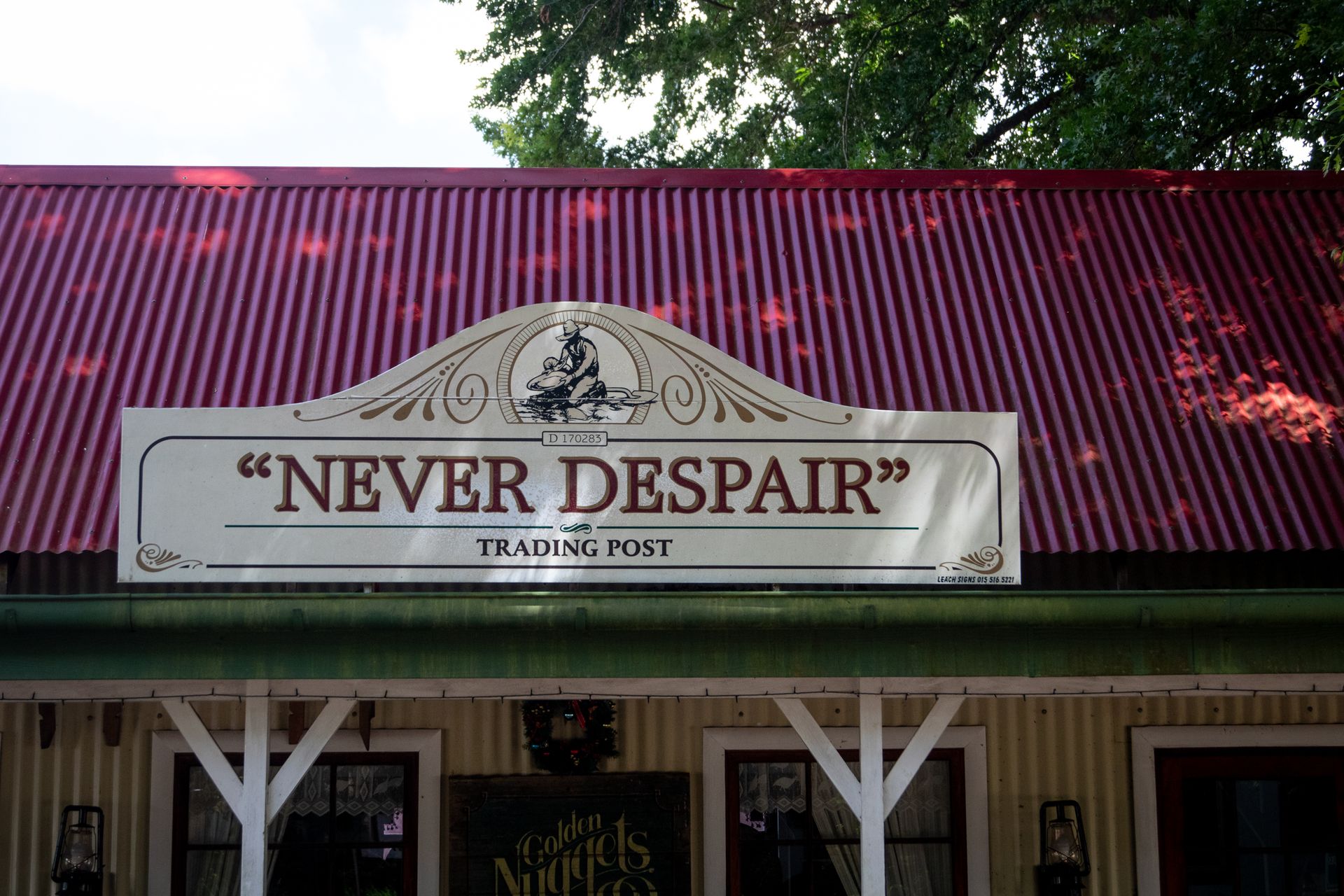 Front view of a quaint trading post with Never Despair sign under a vibrant red roof.