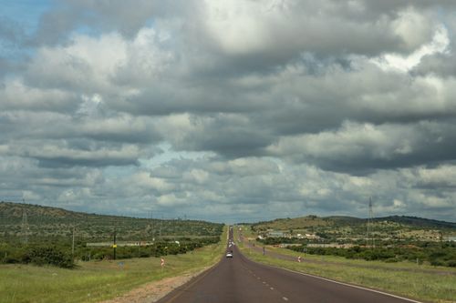 Free Long stretch of highway through countryside with dramatic cloud-filled sky. Stock Photo