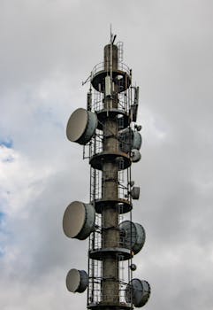 A vertical telecommunication tower with satellite dishes against a cloudy sky.