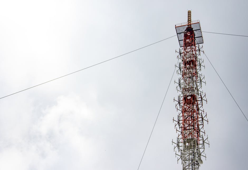 A towering red and white telecommunications structure reaching into a cloudy sky, highlighting modern technology.