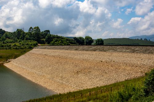 Free Tranquil rural landscape featuring a dam and lush greenery under a bright sky. Stock Photo