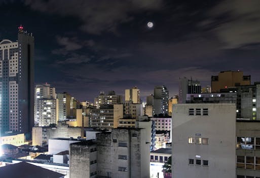 Vibrant city nightscape with a full moon and illuminated skyscrapers.