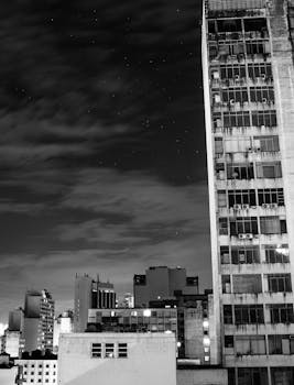 Discover the striking contrast of city skyscrapers against a starry night sky in black and white.