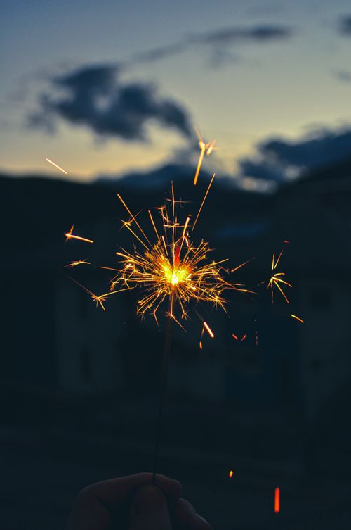 Free A hand holding a bright sparkler against a dusky evening sky, creating a vivid, festive ambiance. Stock Photo