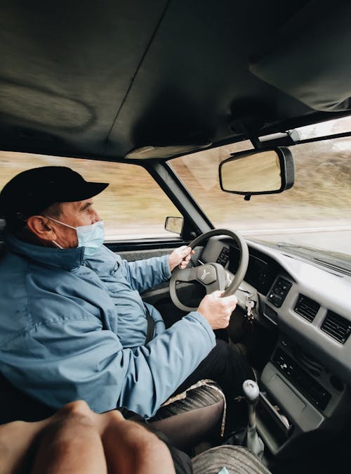 Elderly Man in a Face Mask Driving a Car 
