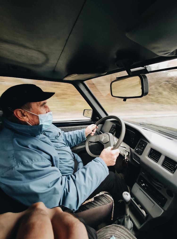 Elderly Man In A Face Mask Driving A Car 