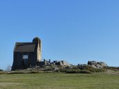 Aged house on grassy hill under clear blue sky