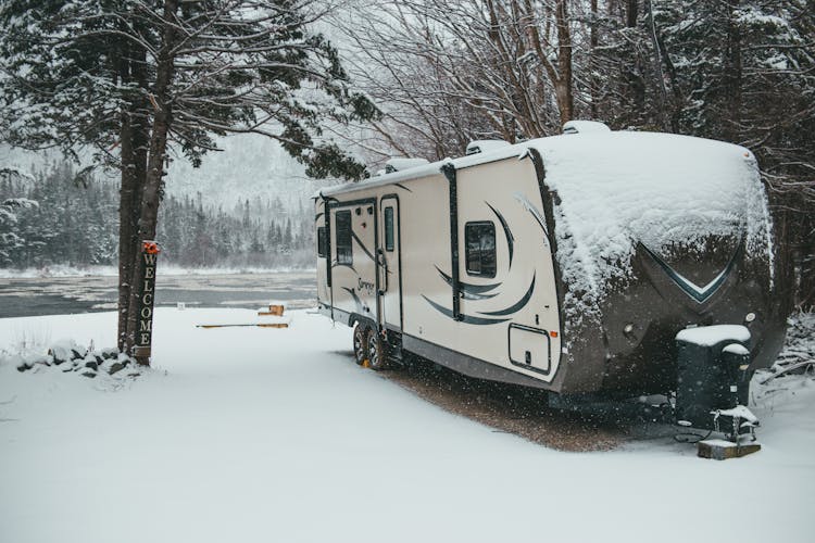 Travel Trailer Placed Near River In Winter Forest In Daylight