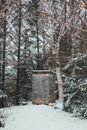 Facade of old small warm shack with snowy roof surrounded by tall coniferous and leafless deciduous trees in woods in winter