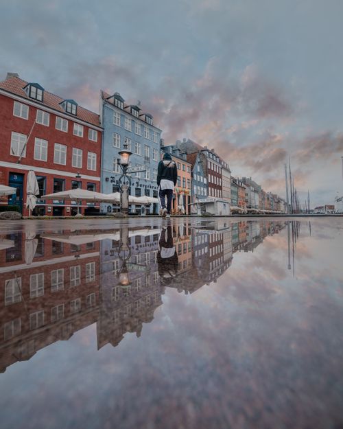 Free A person walking along the Nyhavn waterfront in Copenhagen, Denmark, reflected in a puddle. Stock Photo