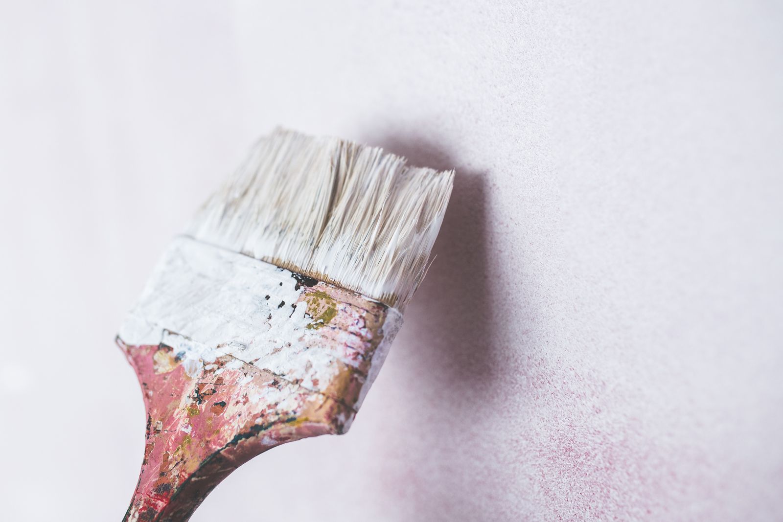 Painter applying Sandtex masonry paint to an exterior wall with a brush