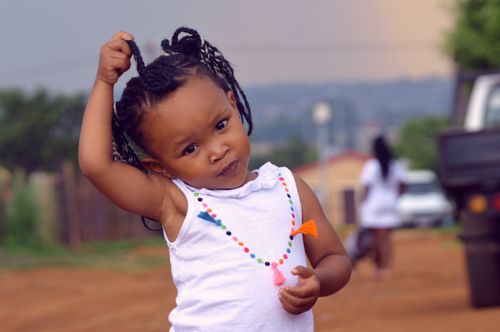 Free Cute child portrait with braided hair standing on a sunny day in a colorful necklace. Stock Photo
