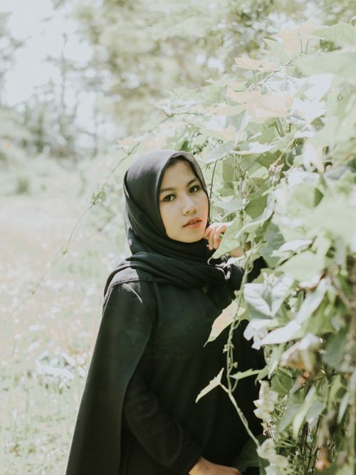 Free A serene portrait of a woman in a black hijab surrounded by lush green foliage outdoors. Stock Photo