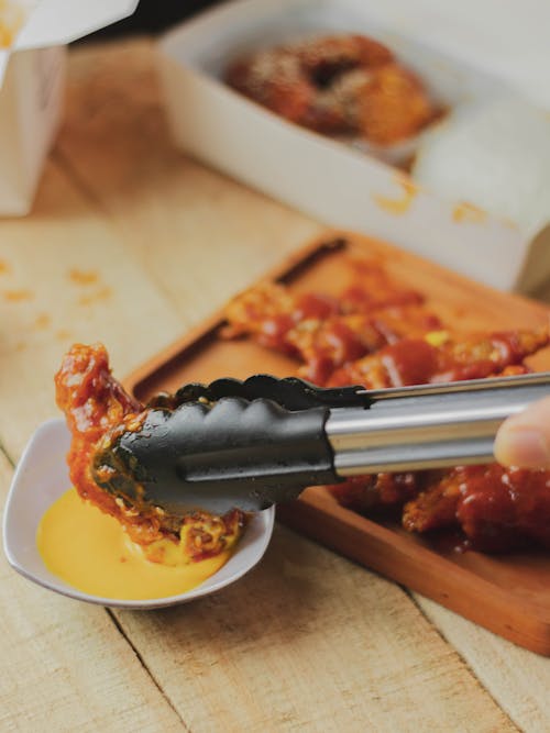 A Person Dipping a Spicy Chicken in a Yellow Sauce with a Tongs