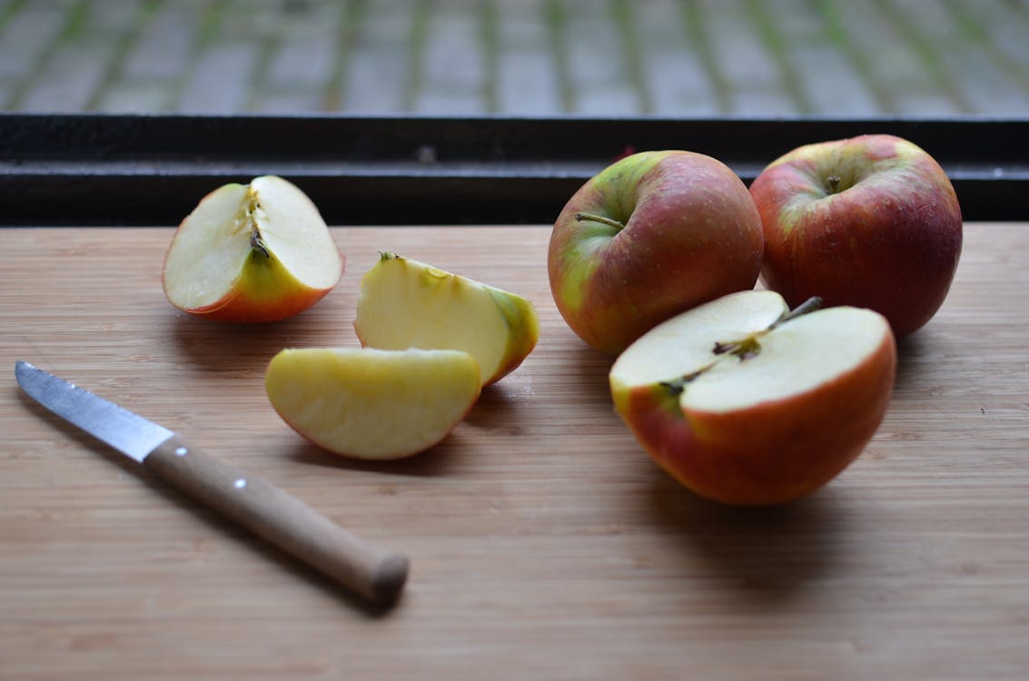 Board with slices of fresh apples and knife near window