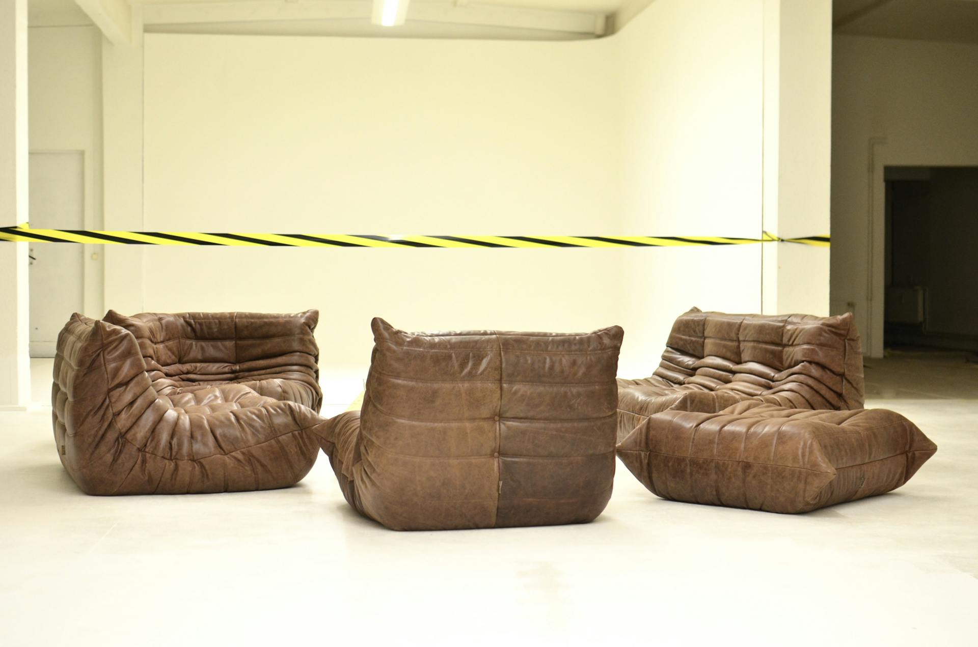 Leather couches placed in empty room under bright striped barrier tape during renovation process