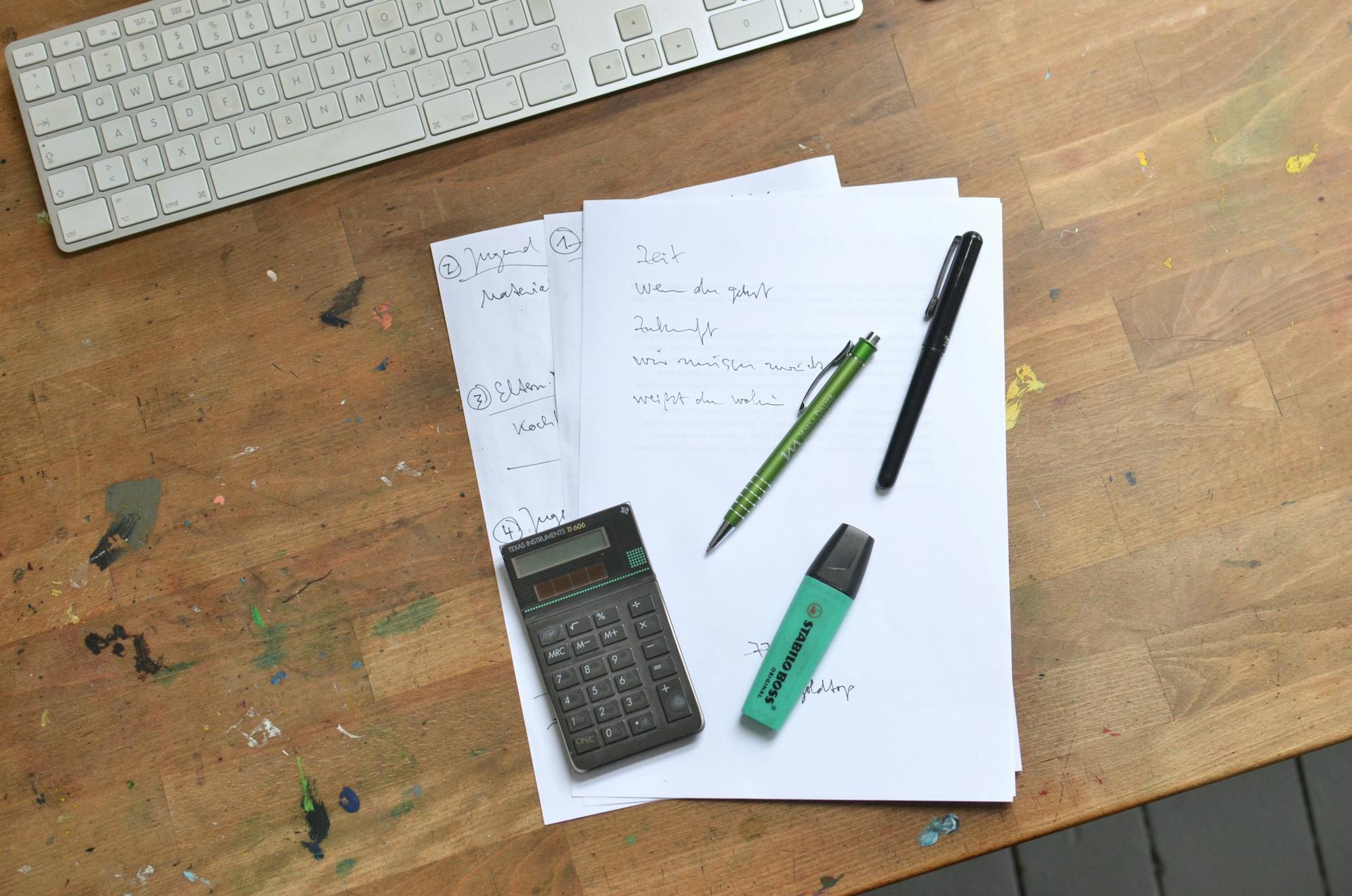 Overhead view of office desk with paperwork, calculator, keyboard, and stationery supplies for work organization.