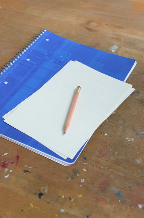 Free From above of bound spiral notebook with blank paper sheets and pencil placed on dirty wooden table Stock Photo